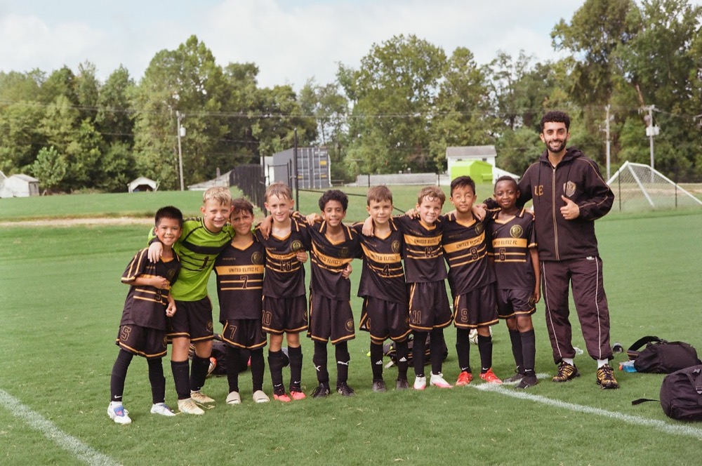 United Elitez FC players and their coach posing together with their arms around each other on the field